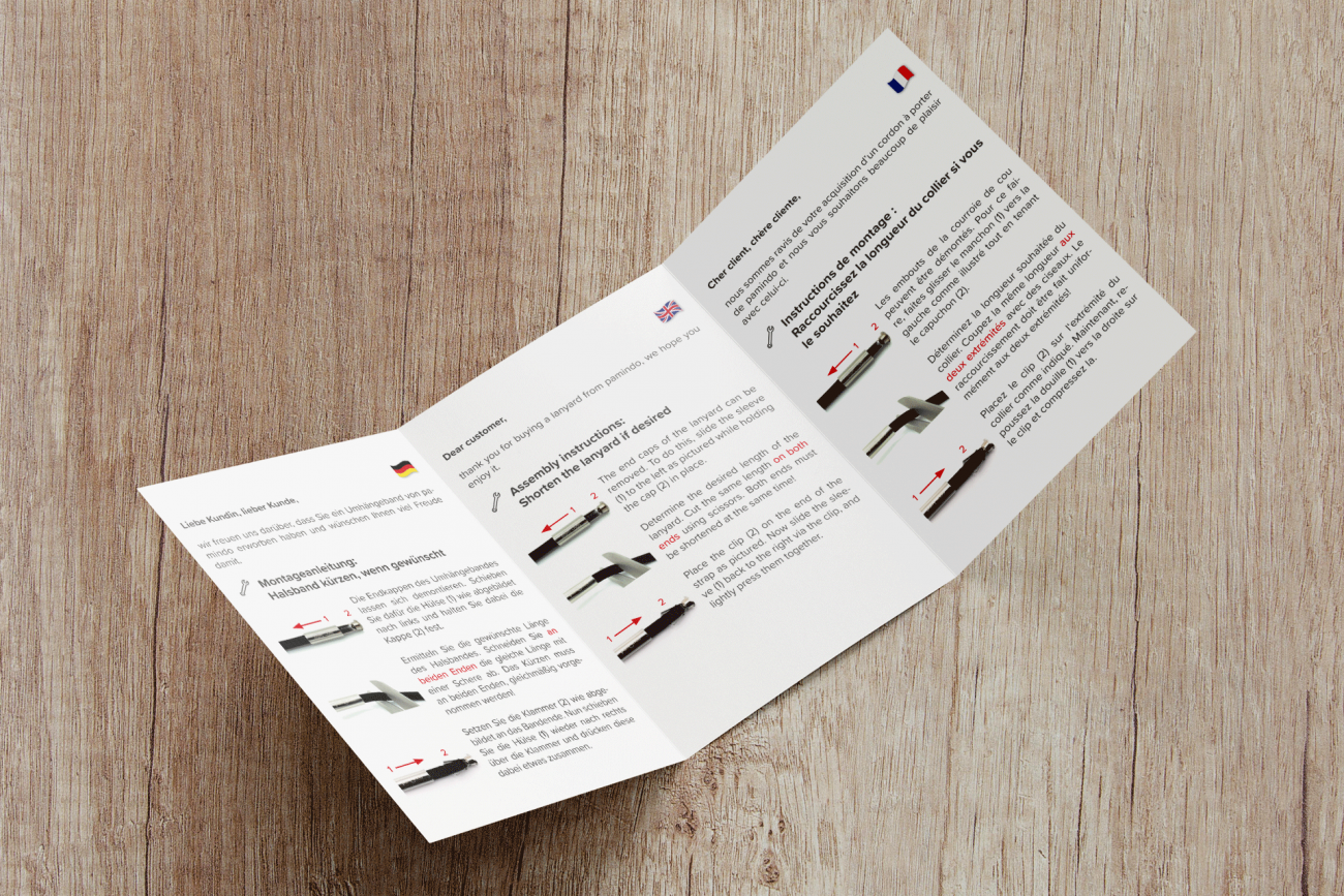 Aufgeschlagener A6 Flyer der eine Montageanleitung für eine Handykette in verschiedenen Sprachen beinhaltet.