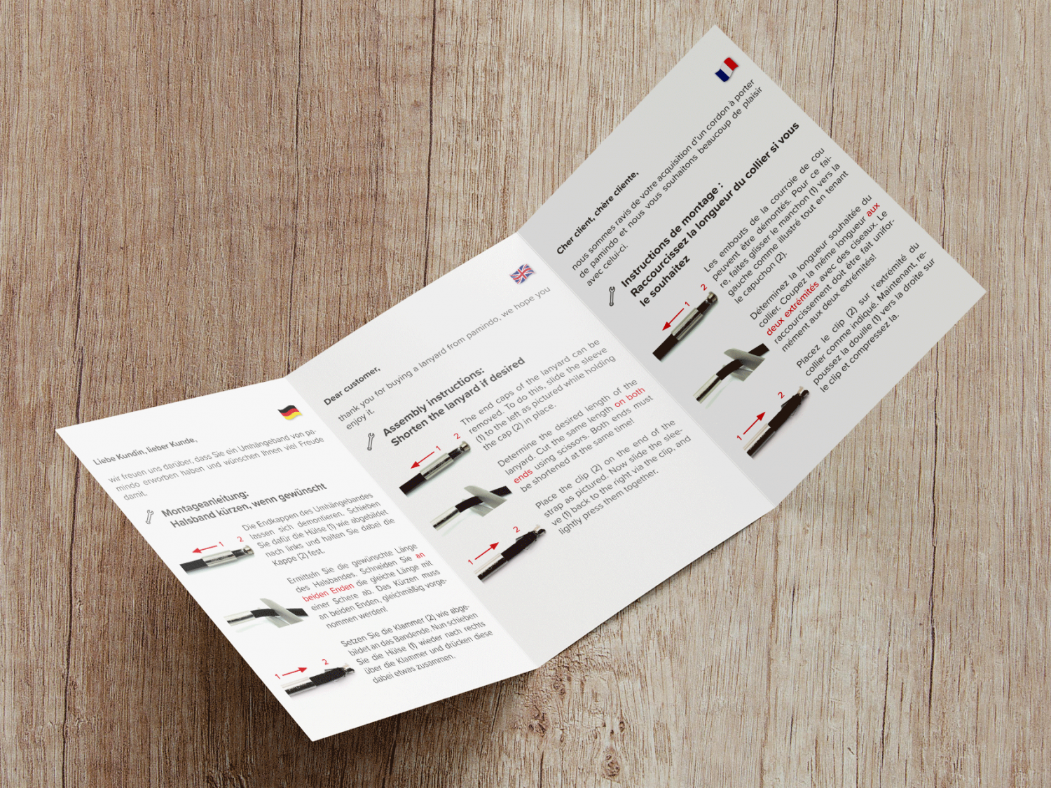 Aufgeschlagener A6 Flyer der eine Montageanleitung für eine Handykette in verschiedenen Sprachen beinhaltet.